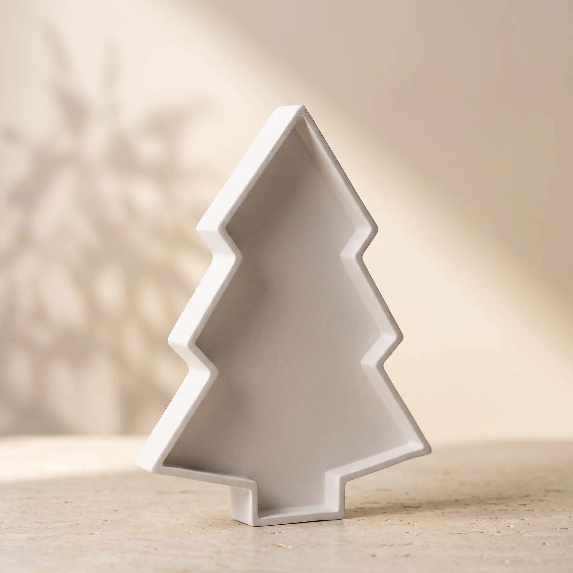 Bandeja decorativa de yeso blanco mate con forma de silueta de árbol de Navidad sobre superficie de piedra clara