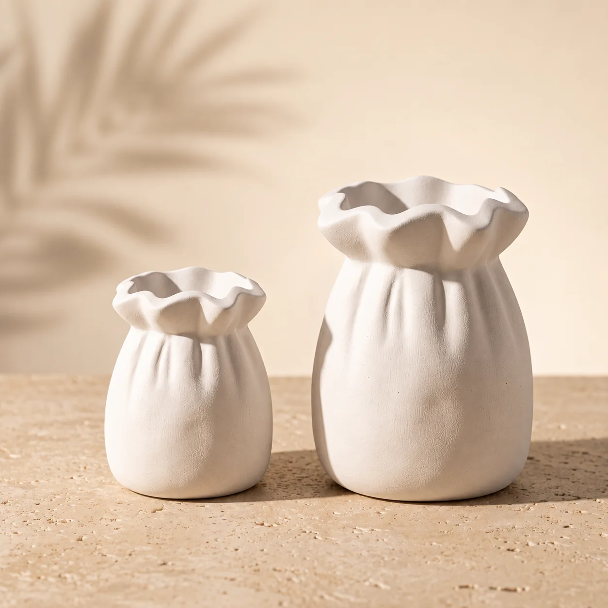 Florero decorativo artesanal de yeso blanco mate con forma de bolsa plisada en tamaños de 8 cm y 12 cm sobre superficie de piedra
