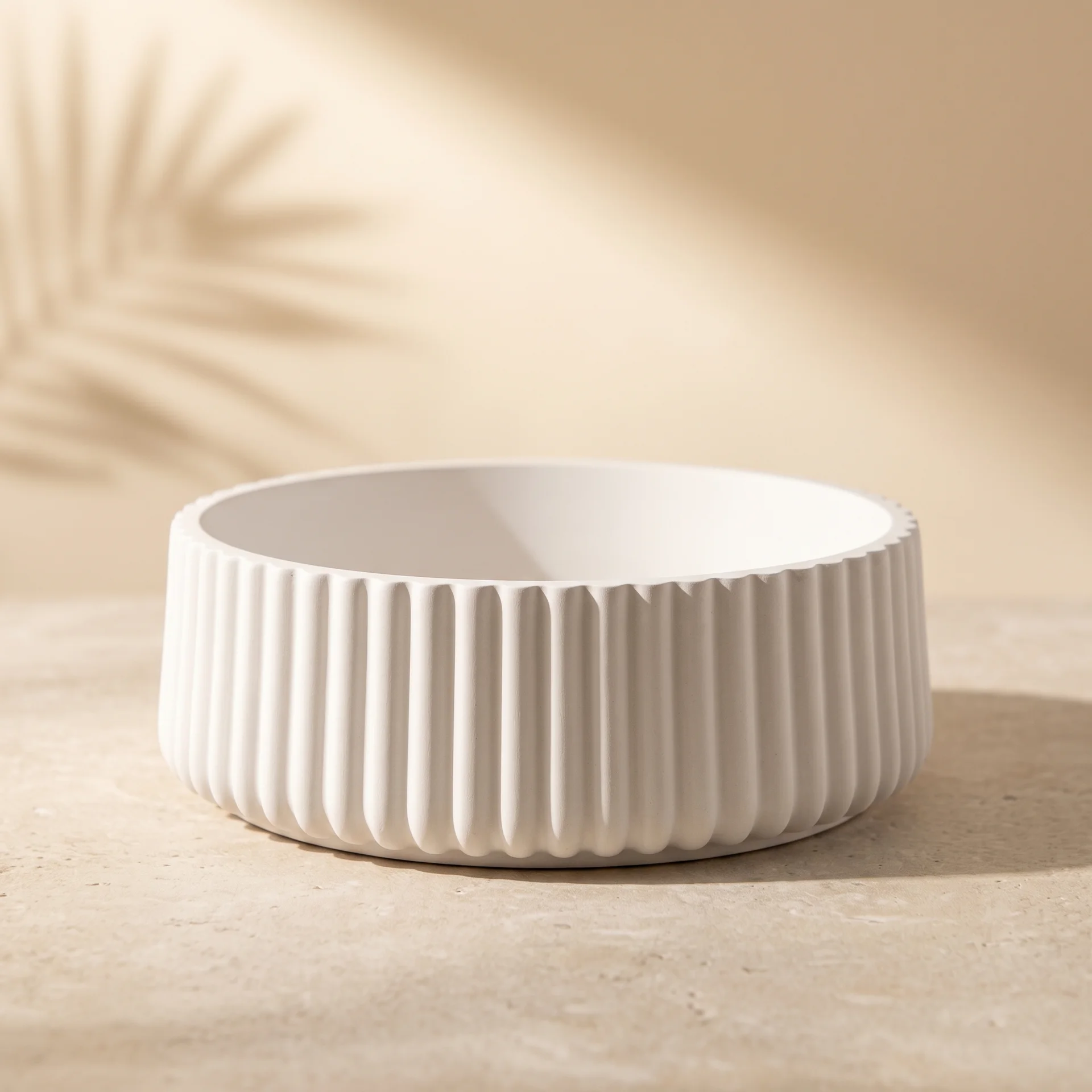 Cuenco circular de yeso cerámico blanco con relieve acanalado sobre superficie de piedra clara estilo nórdico